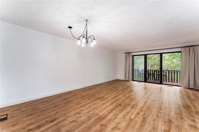 empty room featuring a textured ceiling, a chandelier, visible vents, baseboards, and light wood-type flooring