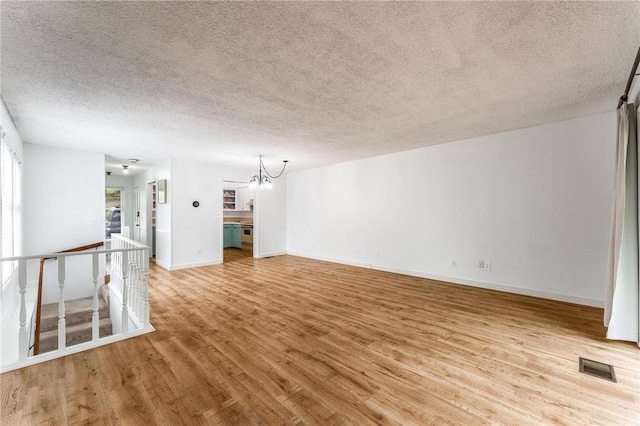 unfurnished living room with a textured ceiling, visible vents, a chandelier, and light wood-style floors