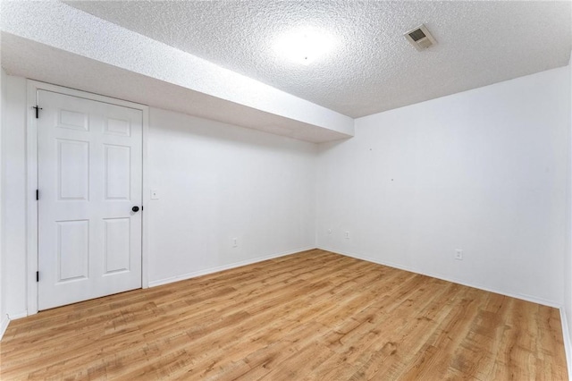 finished below grade area featuring a textured ceiling, light wood-style floors, and baseboards