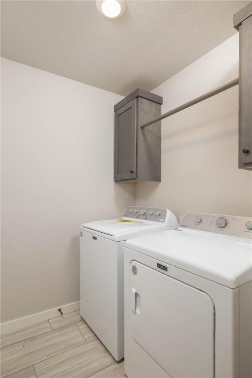 clothes washing area featuring cabinet space, washing machine and clothes dryer, light wood-style flooring, and baseboards