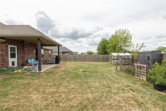 view of yard with a fenced backyard, a patio area, an outbuilding, and a greenhouse