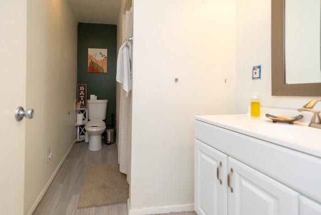bathroom featuring toilet, baseboards, wood finished floors, and vanity