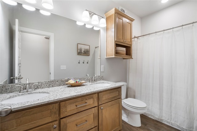 full bath with a sink, double vanity, toilet, and wood finished floors