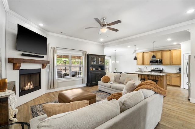 living room with light wood-type flooring, a ceiling fan, crown molding, and a fireplace