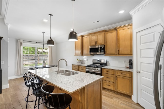 kitchen featuring a kitchen island with sink, a breakfast bar area, a sink, light wood-style flooring, and stainless steel appliances