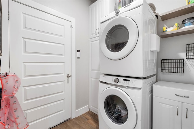 washroom featuring stacked washing maching and dryer, baseboards, cabinet space, and wood finished floors