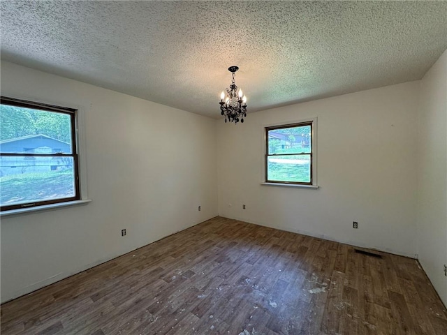 unfurnished room featuring a textured ceiling, a chandelier, wood finished floors, and visible vents
