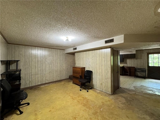 below grade area featuring wood walls, a textured ceiling, and visible vents