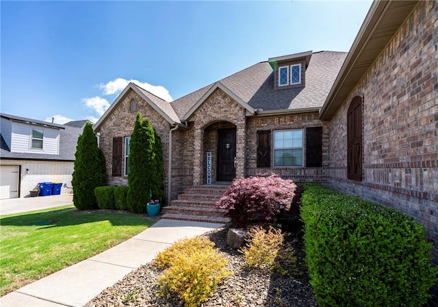 view of front of house featuring roof with shingles, a front yard, and brick siding