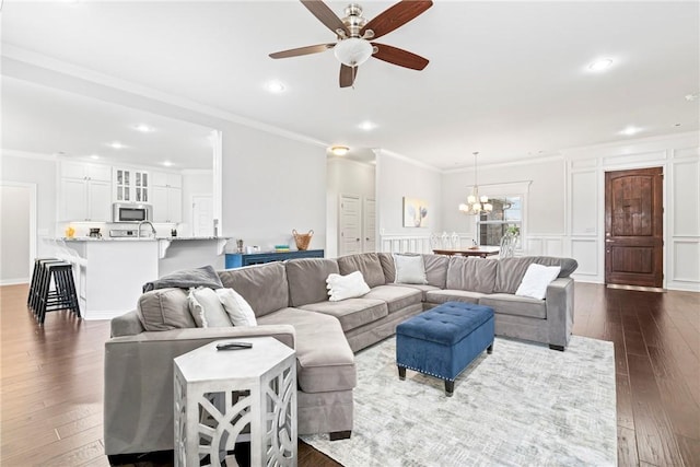 living room with crown molding, ceiling fan with notable chandelier, and dark wood-type flooring