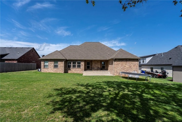 back of house featuring a lawn, a trampoline, and brick siding