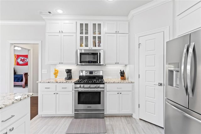 kitchen featuring visible vents, ornamental molding, white cabinets, tasteful backsplash, and stainless steel appliances