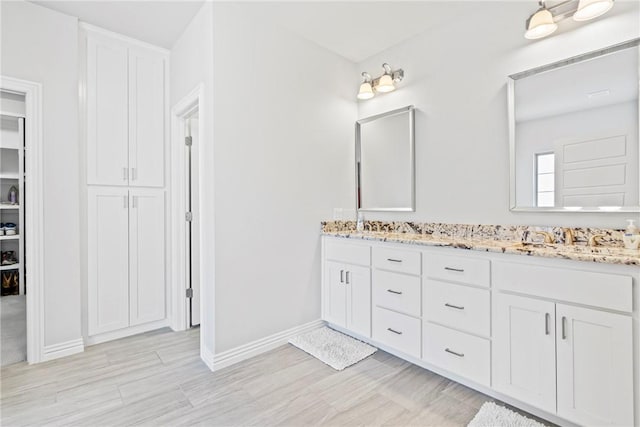 full bath featuring baseboards, double vanity, wood finished floors, and a closet