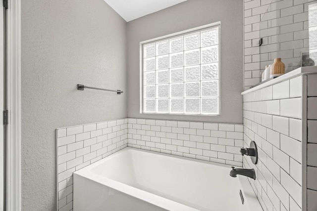bathroom featuring a textured wall and a bath