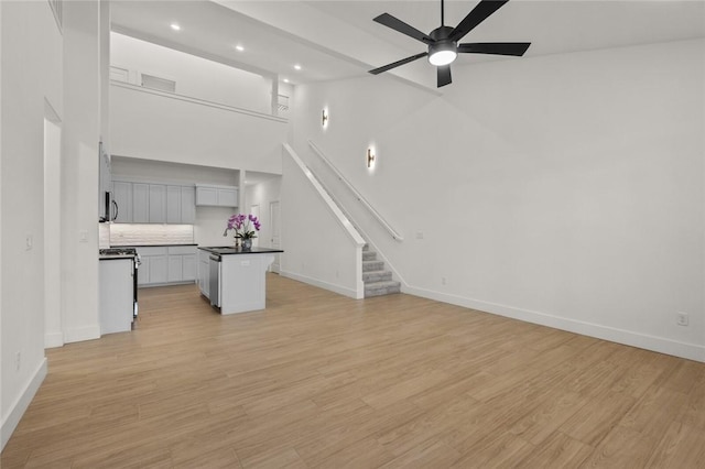 unfurnished living room featuring baseboards, a ceiling fan, and stairs