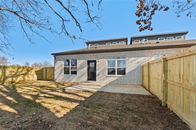 rear view of property with brick siding, a fenced backyard, and a patio area