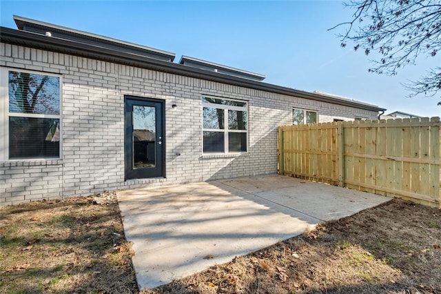 rear view of house with brick siding, a patio area, and fence