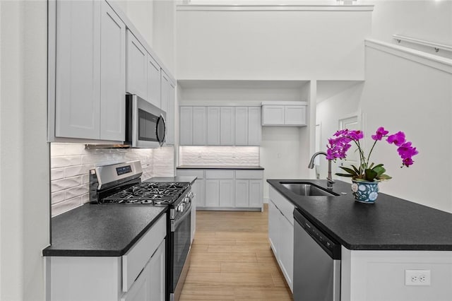 kitchen with a sink, dark countertops, appliances with stainless steel finishes, and light wood-style flooring