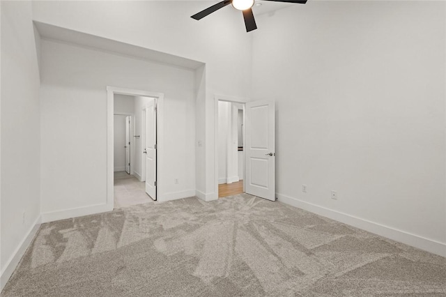 unfurnished bedroom featuring carpet, a ceiling fan, baseboards, ensuite bathroom, and a towering ceiling