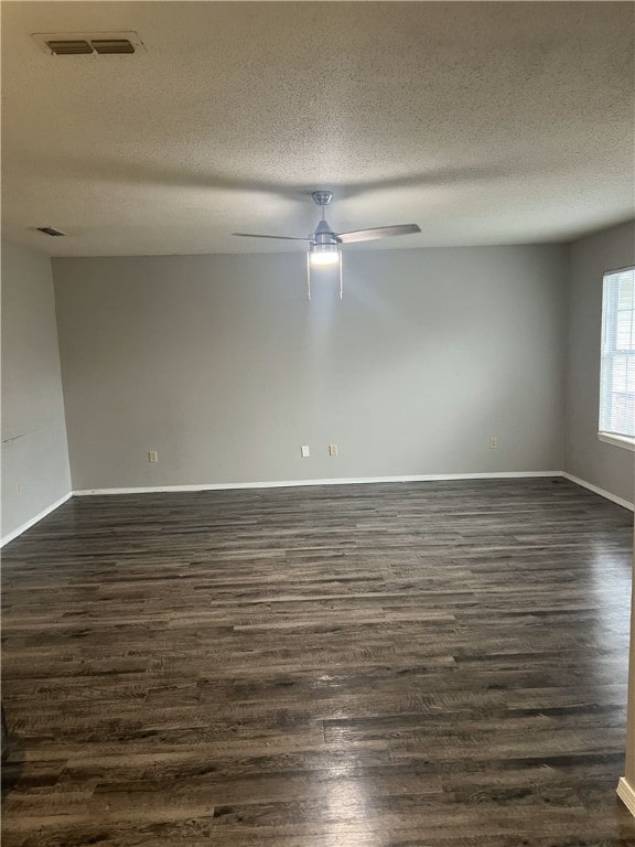empty room featuring ceiling fan, a textured ceiling, visible vents, baseboards, and dark wood-type flooring