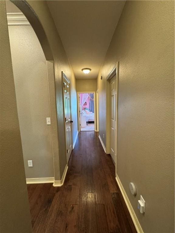 hallway featuring arched walkways, baseboards, and dark wood-type flooring