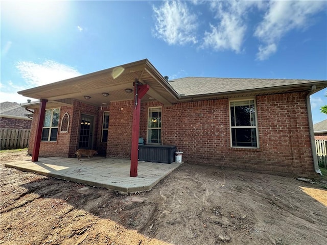 back of property with brick siding, fence, a shingled roof, and a patio area