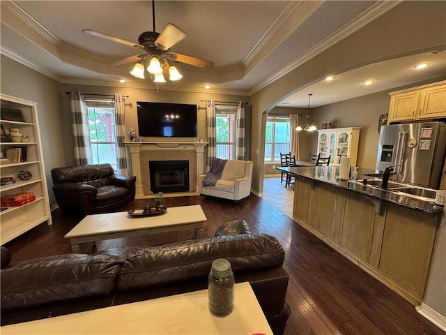 living room featuring ceiling fan, a raised ceiling, a fireplace, arched walkways, and dark wood-style floors