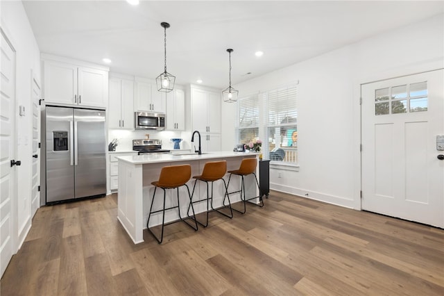 kitchen with a kitchen island with sink, wood finished floors, white cabinets, a sink, and appliances with stainless steel finishes