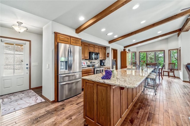 kitchen featuring brown cabinetry, a sink, lofted ceiling with beams, dark wood-style floors, and stainless steel appliances