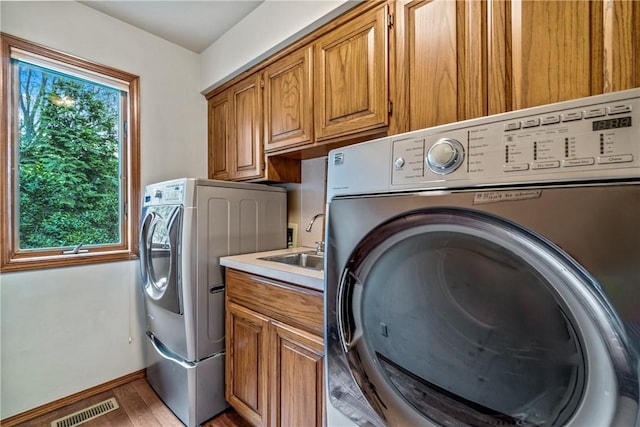 laundry room with cabinet space, washer and clothes dryer, a sink, and light wood-style flooring