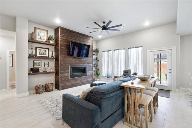 living area featuring ceiling fan, a large fireplace, baseboards, and wood finished floors
