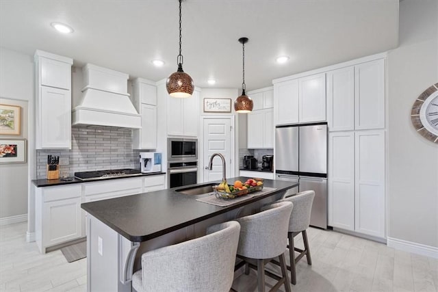 kitchen with appliances with stainless steel finishes, tasteful backsplash, a sink, premium range hood, and baseboards