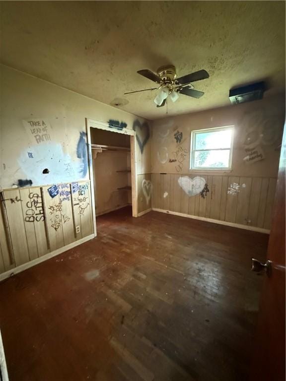empty room with baseboards, a ceiling fan, wainscoting, and dark wood-style floors