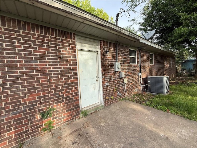 entrance to property featuring central air condition unit, a patio, and brick siding
