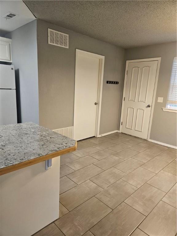 unfurnished dining area with a textured ceiling, baseboards, visible vents, and light tile patterned floors