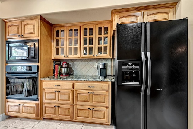 kitchen with decorative backsplash, light stone countertops, glass insert cabinets, light tile patterned floors, and black appliances