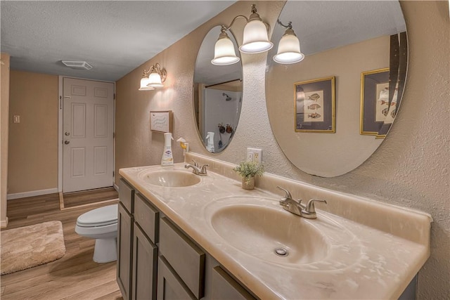 302 4th Ave, Gravette, AR 72736 - full bathroom featuring wood finished floors, toilet, a textured ceiling, a textured wall, and double vanity