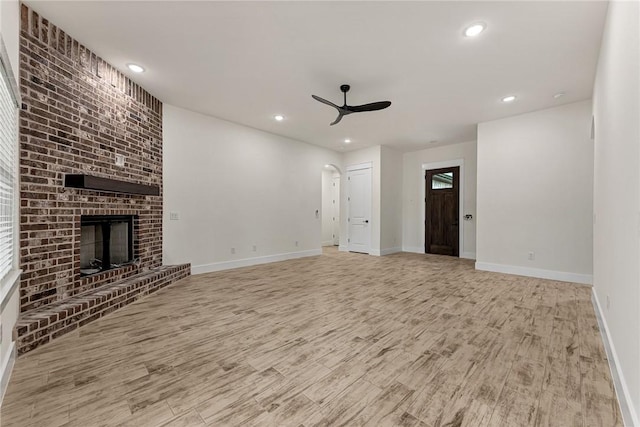 4 Lothian Dr, Bella Vista, AR 72715 - unfurnished living room with a ceiling fan, wood finished floors, baseboards, arched walkways, and a fireplace