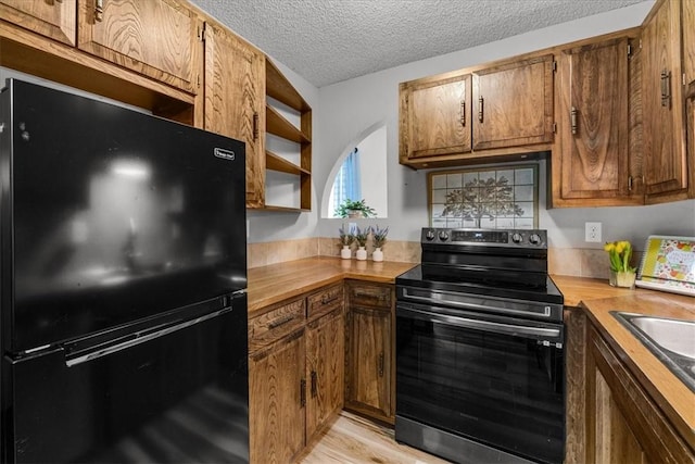 kitchen with butcher block countertops, a textured ceiling, a sink, light wood finished floors, and black appliances