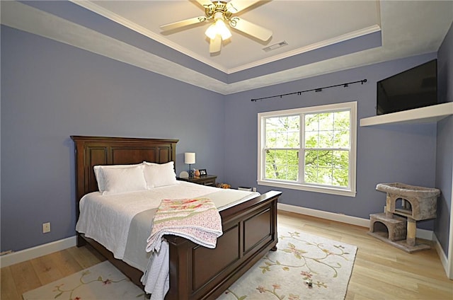 bedroom featuring light wood-type flooring, baseboards, and a tray ceiling