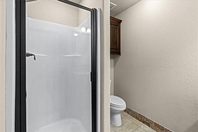 bathroom with baseboards, a textured wall, toilet, and a shower stall