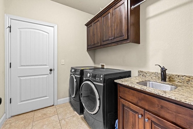 clothes washing area with cabinet space, a sink, baseboards, light tile patterned floors, and washing machine and dryer