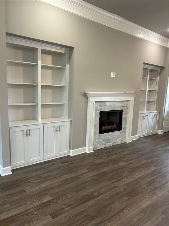 unfurnished living room featuring baseboards, ornamental molding, dark wood-style floors, and a stone fireplace