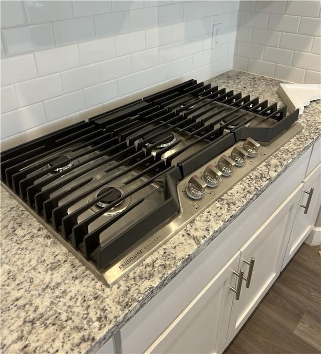 details with decorative backsplash, stainless steel gas cooktop, light stone countertops, white cabinets, and dark wood finished floors