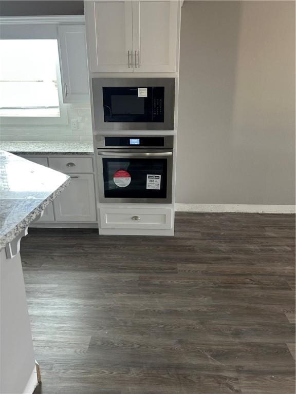 kitchen featuring baseboards, dark wood-style floors, light stone countertops, and oven