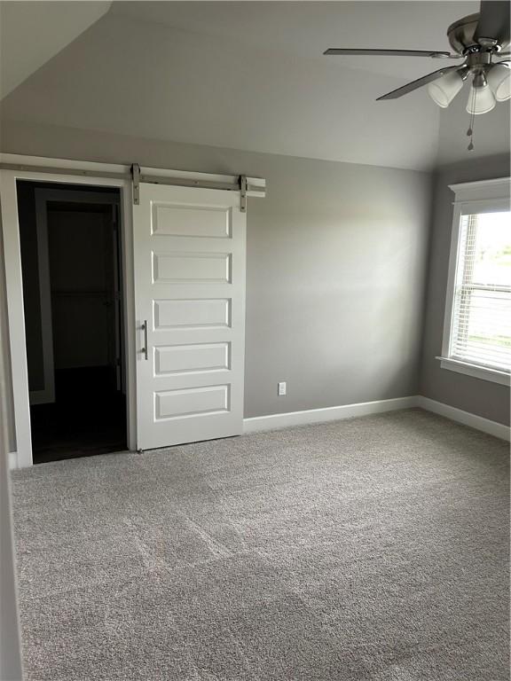 unfurnished room with a barn door, carpet floors, a ceiling fan, baseboards, and vaulted ceiling
