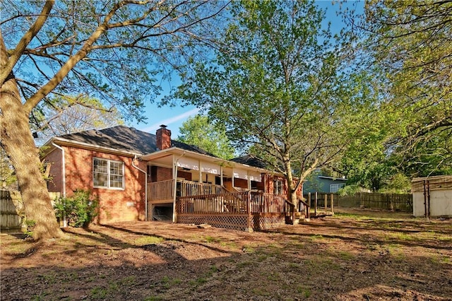 rear view of house with brick siding, a fenced backyard, a chimney, and a deck