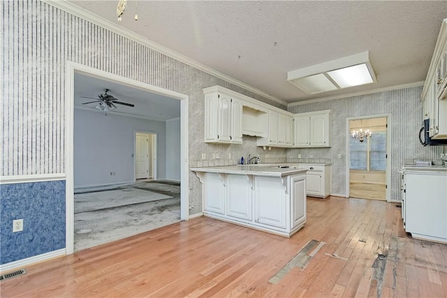 kitchen with crown molding, light countertops, a peninsula, wallpapered walls, and light wood-style flooring