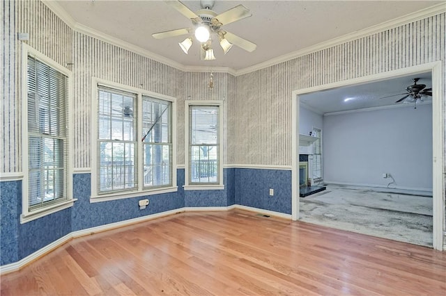spare room with a ceiling fan, a fireplace with raised hearth, ornamental molding, and wood finished floors