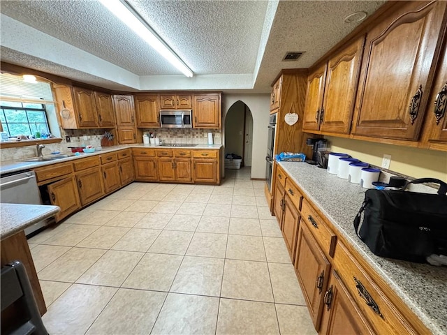 60 N Redwood Cir, Sallisaw, OK 74955 - kitchen with a sink, arched walkways, a textured ceiling, brown cabinetry, and stainless steel microwave